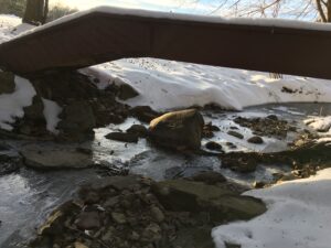 Snow-covered footbridge with icy stream rushing beneath